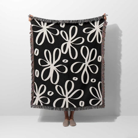 Black and white modern artsy flowers woven blanket throw held by a person on a white background.