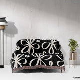 Black and white modern artsy flowers woven blanket throw draped over a couch against a white wall.