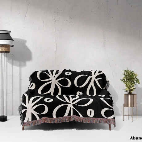 Black and white modern artsy flowers woven blanket throw draped over a couch against a white wall.