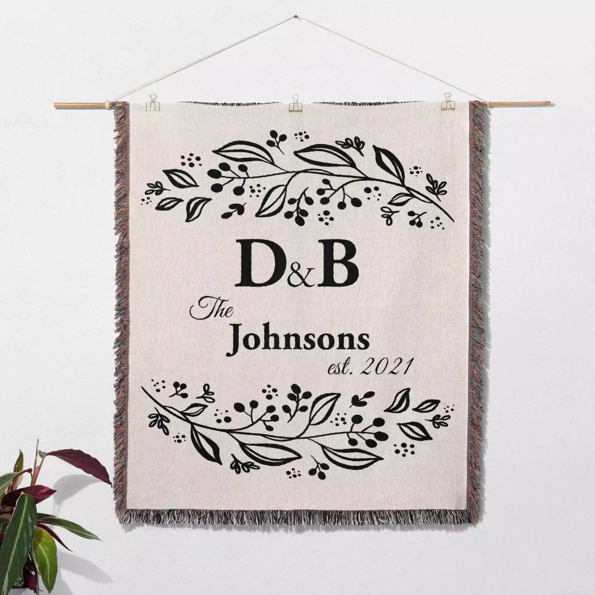Monogrammed cotton throw blanket perfect engagement and wedding gift hanging on a wall on a white background.