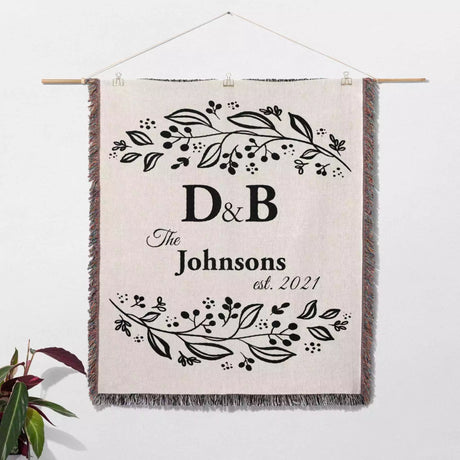 Monogrammed cotton throw blanket perfect engagement and wedding gift hanging on a wall on a white background.