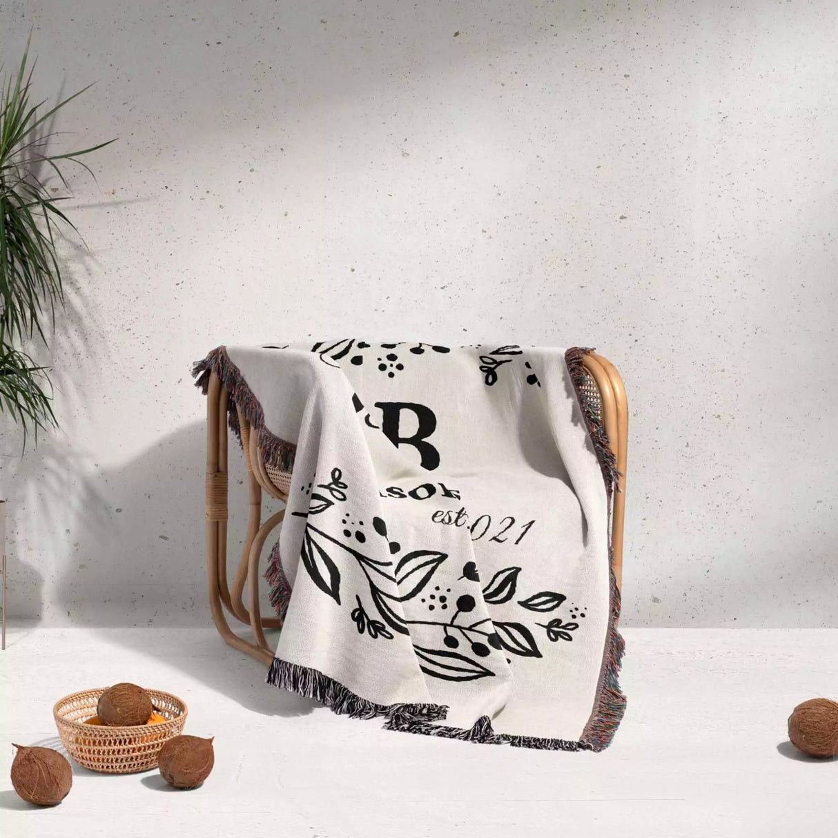 Monogrammed cotton throw blanket perfect engagement and wedding gift draped over a chair on a light background