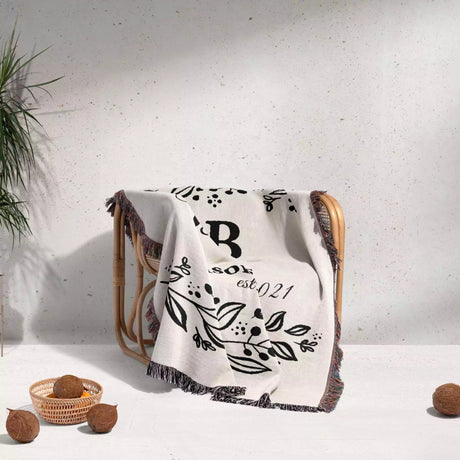 Monogrammed cotton throw blanket perfect engagement and wedding gift draped over a chair on a light background