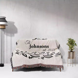Monogrammed cotton throw blanket perfect engagement and wedding gift on a couch against a light gray wall.