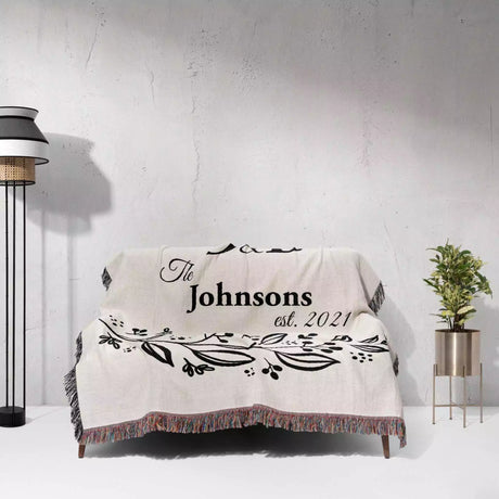 Monogrammed cotton throw blanket perfect engagement and wedding gift on a couch against a light gray wall.