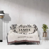 Mr and Mrs cotton wedding anniversary gift woven blanket with 'Mr & Mrs James' and wedding date on a couch against a light gray wall.