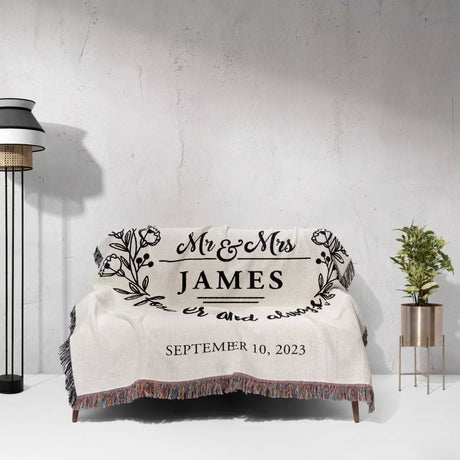 Mr and Mrs cotton wedding anniversary gift woven blanket with 'Mr & Mrs James' and wedding date on a couch against a light gray wall.