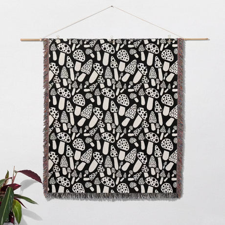 Black and white mushrooms patterned woven blanket throw with fringe hanging on a white wall.