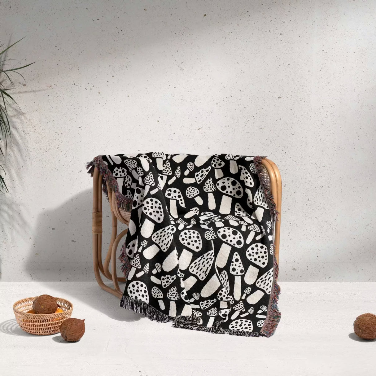 Black and white mushrooms patterned woven blanket throw draped over a wooden chair against a light gray wall.