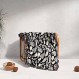 Black and white mushrooms patterned woven blanket throw draped over a wooden chair against a light gray wall.
