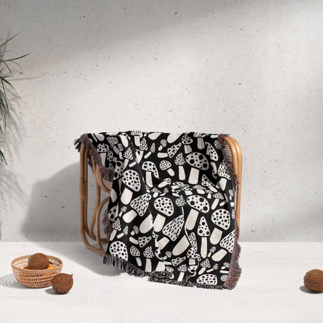 Black and white mushrooms patterned woven blanket throw draped over a wooden chair against a light gray wall.