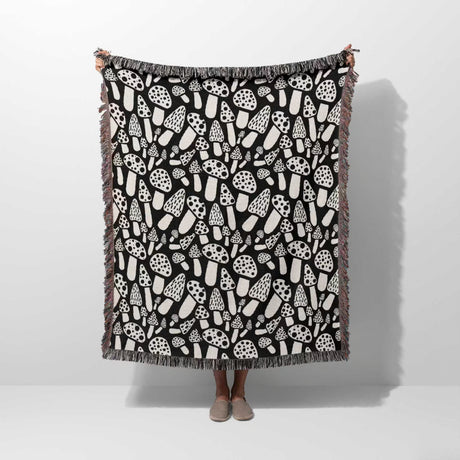 Person holding a black and white mushrooms patterned woven blanket throw against a white background.