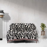 Black and white mushrooms patterned woven blanket throw draped over a sofa against a white wall.