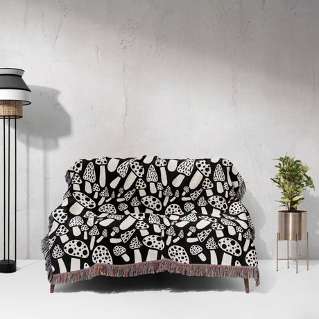 Black and white mushrooms patterned woven blanket throw draped over a sofa against a white wall.