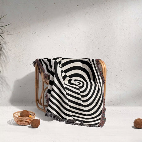 Black and white optical illusion hole woven blanket throw tapestry draped over a chair against a light gray wall.