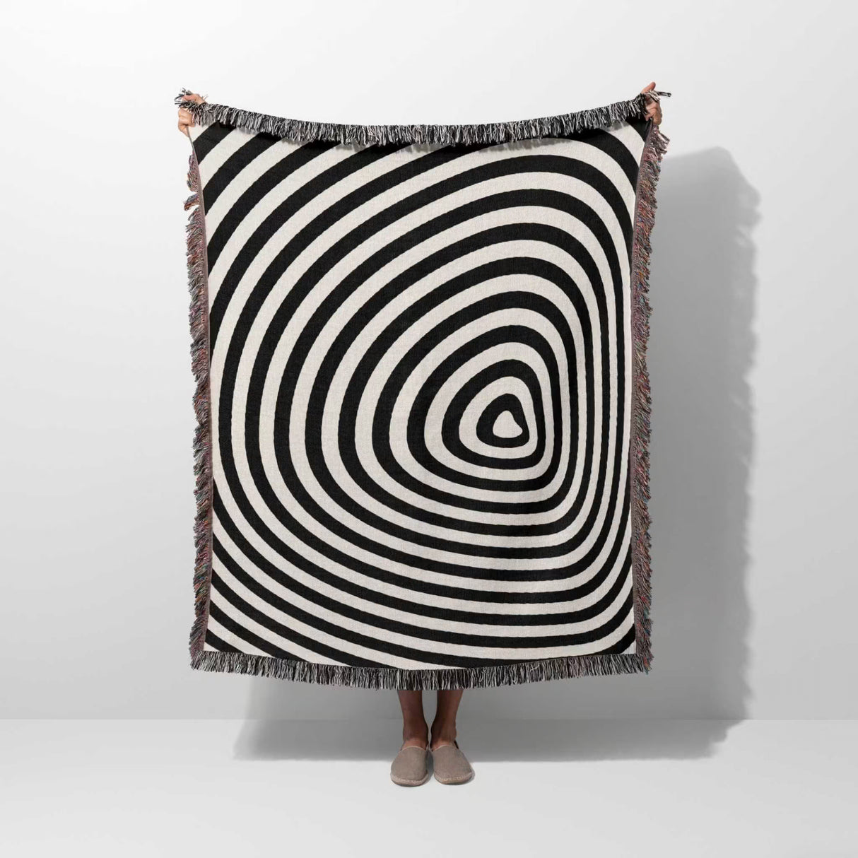 Black and white optical illusion hole woven blanket throw tapestry held by a person on a white background.