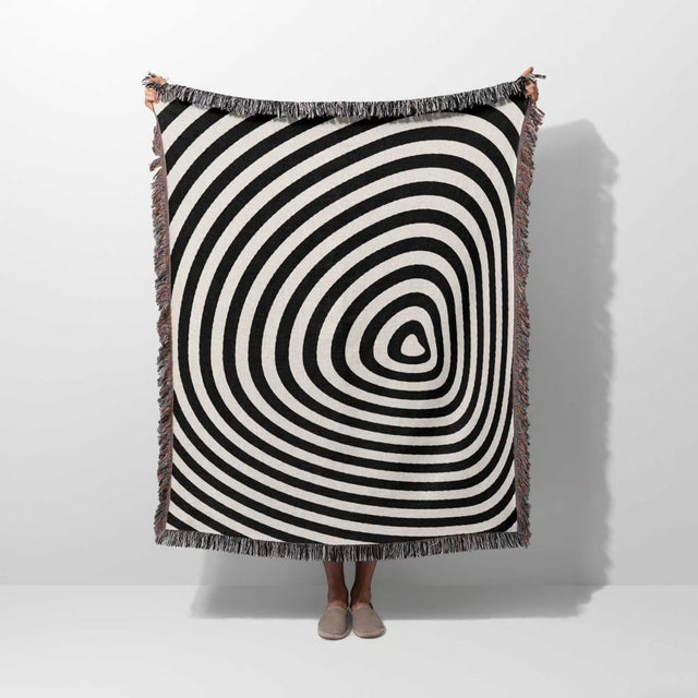 Black and white optical illusion hole woven blanket throw tapestry held by a person on a white background.