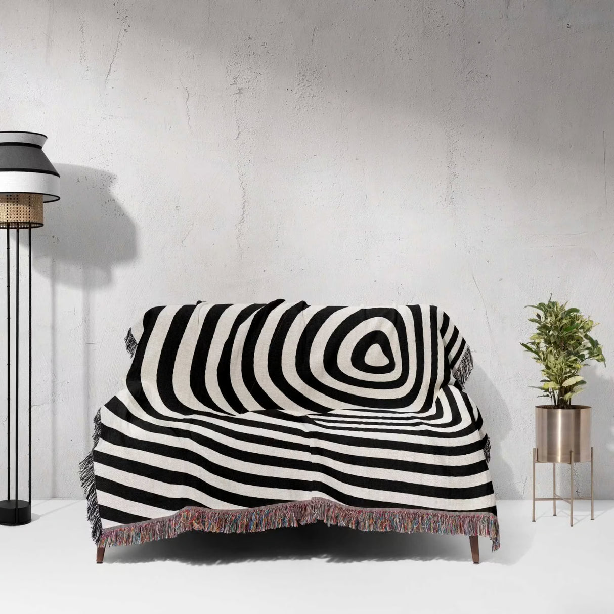 Black and white optical illusion hole woven blanket throw tapestry draped over a couch against a white wall.