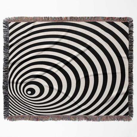 Black and white optical illusion wormhole woven blanket throw tapestry with fringed edges flat lay on a white background.
