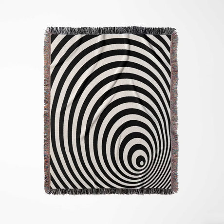 Black and white optical illusion wormhole woven blanket throw tapestry with fringes full view on a light gray background.