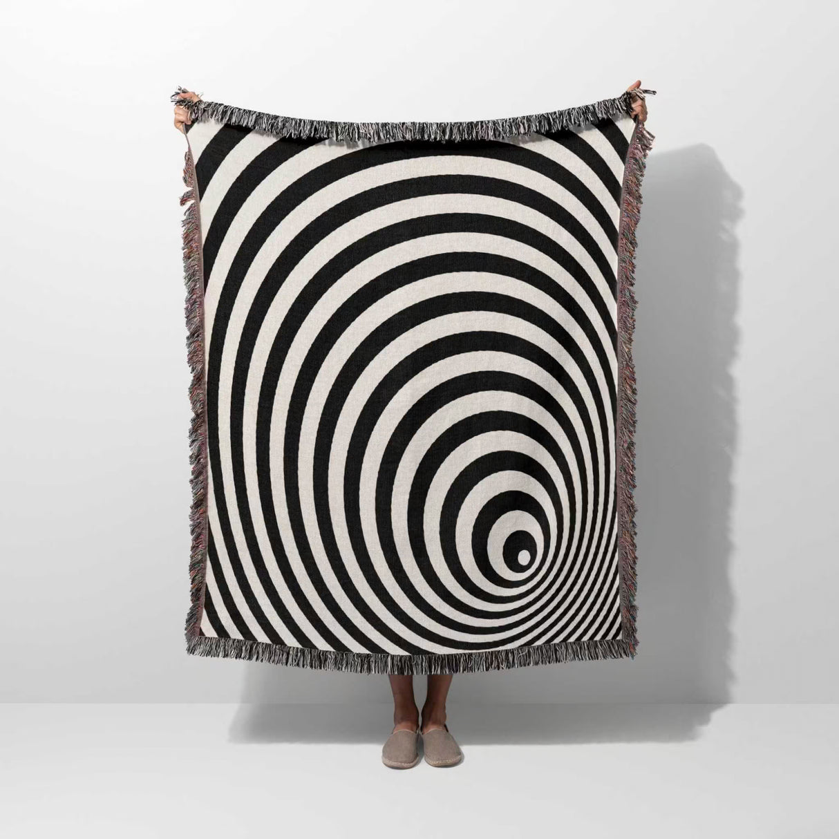 Black and white optical illusion wormhole woven blanket throw tapestry draped over a person on a white background.