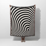 Black and white optical illusion wormhole woven blanket throw tapestry draped over a person on a white background.