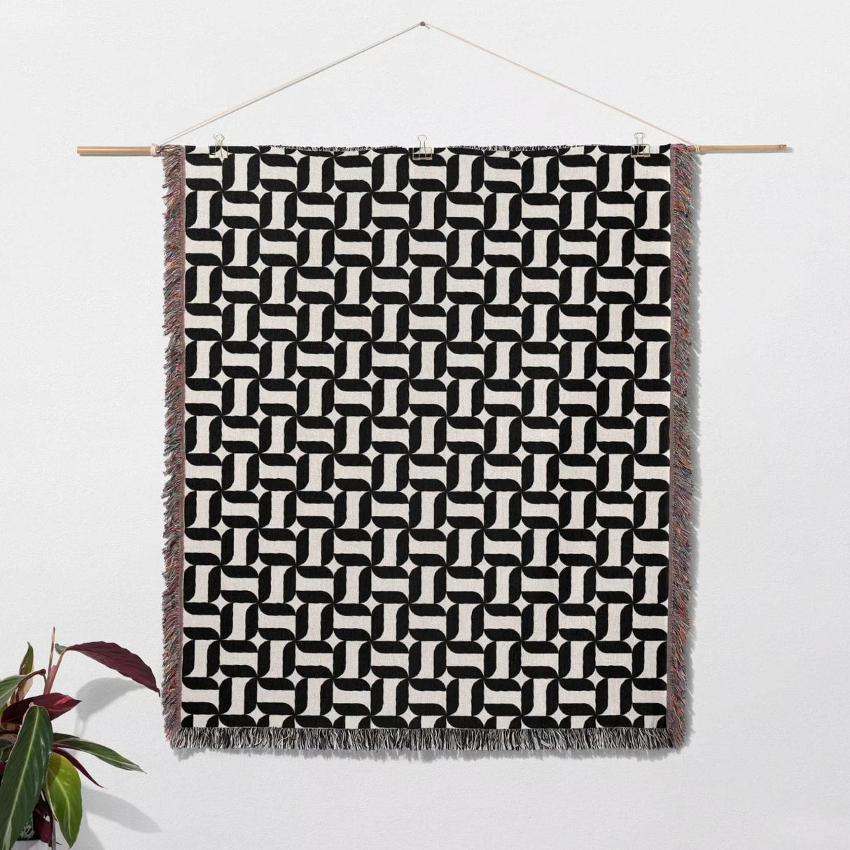 Black and white patterned geometric woven blanket throw tapestry hanging on a wooden rod against a white wall.
