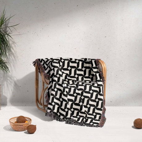 Black and white patterned geometric woven blanket throw tapestry on a wooden chair against a light gray wall.