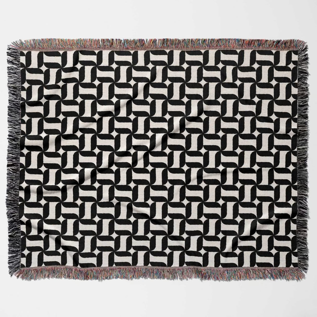 Black and white patterned geometric woven blanket throw tapestry with fringes flat lay on a light gray background.