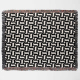 Black and white patterned geometric woven blanket throw tapestry with fringes flat lay on a light gray background.