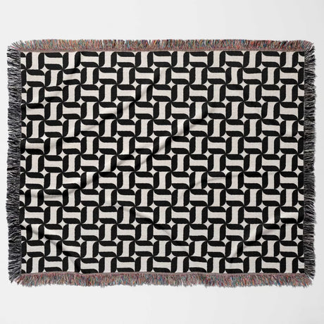 Black and white patterned geometric woven blanket throw tapestry with fringes flat lay on a light gray background.