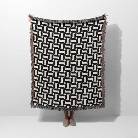 Black and white patterned geometric woven blanket throw tapestry held by a person on a white background.