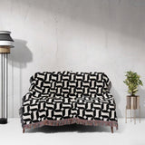 Black and white patterned geometric woven blanket throw tapestry draped over a couch against a white wall.