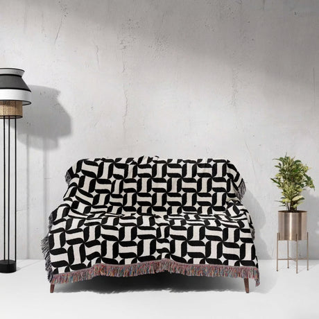 Black and white patterned geometric woven blanket throw tapestry draped over a couch against a white wall.
