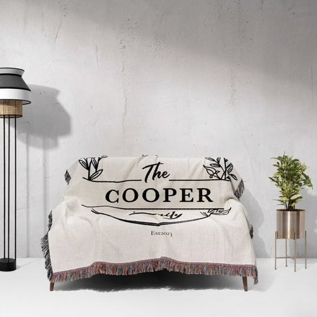 Personalized 2 year anniversary gift for wife woven throw blanket with 'The Cooper Family' text draped over a couch against a white wall.
