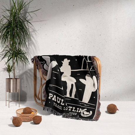 Personalized cowboy and cowgirl 2nd anniversary gift woven throw blanket with custom text draped over a chair, with a plant and coconuts in the background.