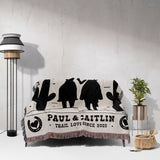 Personalized cowboy and cowgirl cotton anniversary gift woven throw blanket with black silhouettes and text draped over a couch in a room with a lamp and plant.