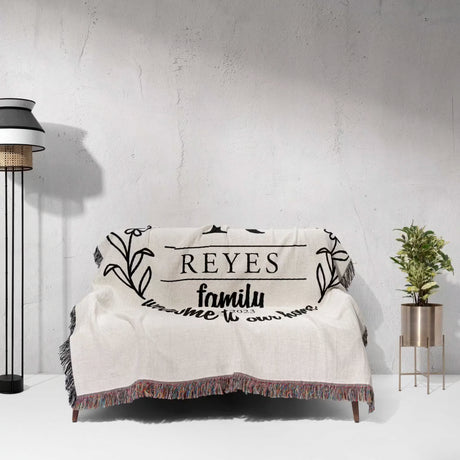Personalized family name woven blanket rustic home décor gift with 'REYES family' text draped over a couch against a light gray wall.
