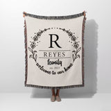 Personalized family name woven blanket rustic home décor gift with 'REYES family welcome to our home' text hold by a person on a white background