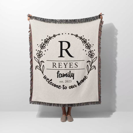 Personalized family name woven blanket rustic home décor gift with 'REYES family welcome to our home' text hold by a person on a white background