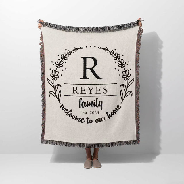 Personalized family name woven blanket rustic home décor gift with 'REYES family welcome to our home' text hold by a person on a white background