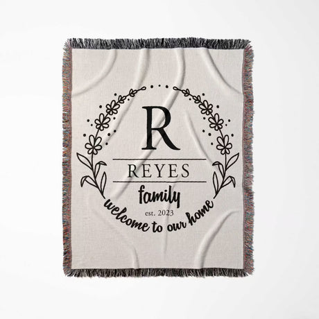 Personalized family name woven blanket rustic home décor gift with 'Reyes family, welcome to our home' text flat lay on a white background