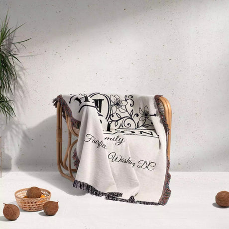 Personalized family name and address blanket with decorative text and patterns draped over a chair on a light background