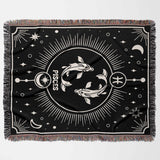 A flat horizontal image of the Pisces Zodiac Blanket showcasing the intricate black and white design. The blanket features two fish, a symbol of the Pisces zodiac, surrounded by celestial elements and detailed fringe edges.