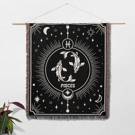 The Pisces Zodiac Blanket is hung on a wall as decor, demonstrating its versatility. The blanket's detailed black and white design with the Pisces symbol is showcased as an artistic piece.