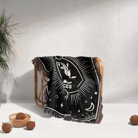 Image shows the Pisces Zodiac Blanket draped over a chair in a cozy setting. The blanket's black and white design with the Pisces zodiac symbol is visible, adding a stylish touch to the decor.