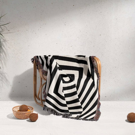 Psychedelic abstract art woven blanket throw tapestry draped over a chair against a light gray wall.
