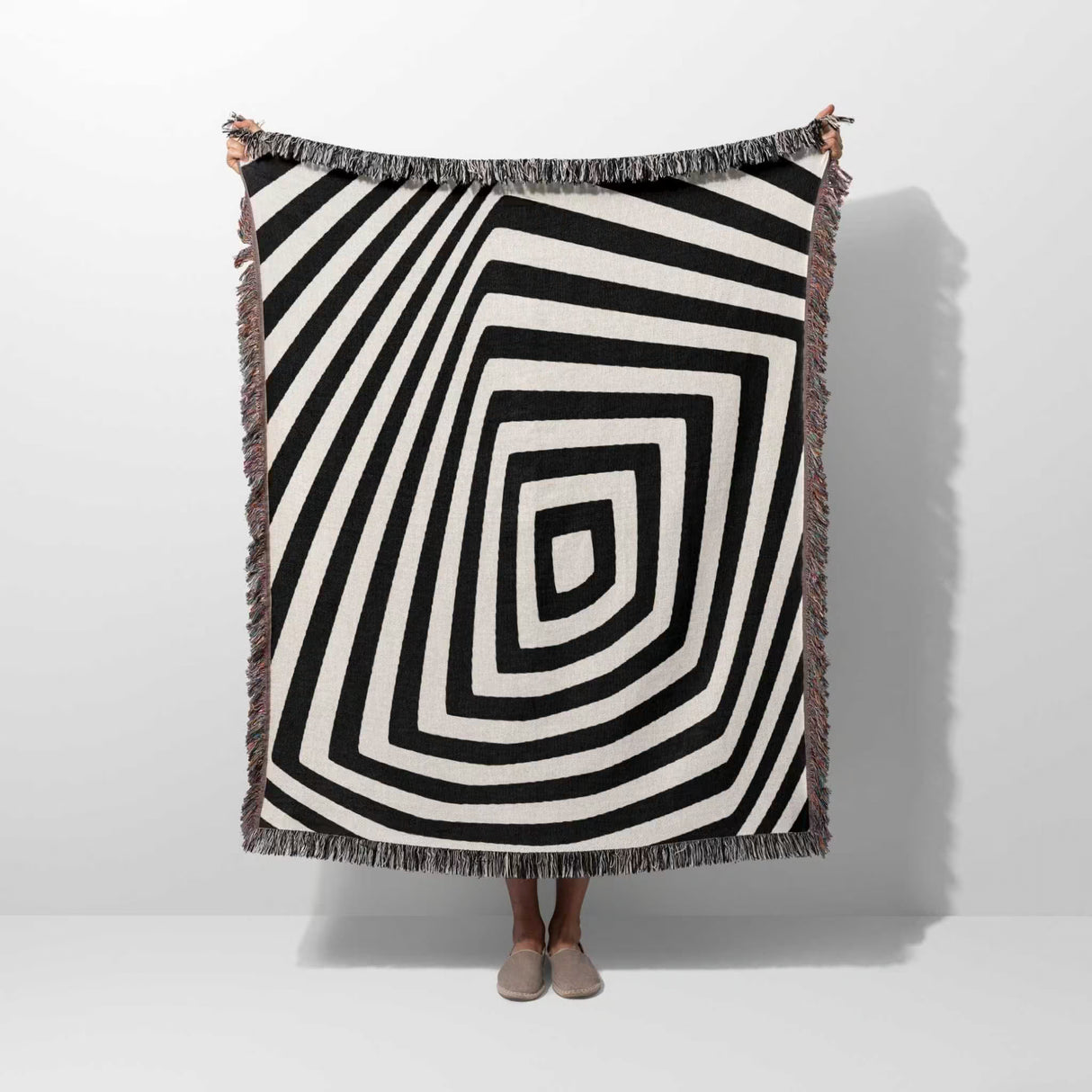 Psychedelic abstract art woven blanket throw tapestry with a person partially visible underneath on a white background.