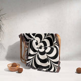 Black and white psychedelic flower woven blanket throw tapestry draped over a chair against a light gray background.