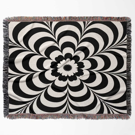 Black and white psychedelic flower woven blanket throw tapestry with fringed edges horizontal flat lay on a white background.